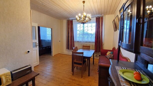 Ein Essbereich mit Holztisch und Stühlen, einer Kandelaberleuchte und einem mit Vorhängen versehenen Fenster.
