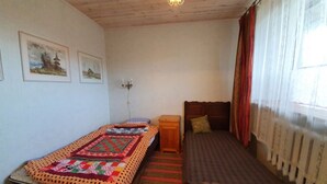 Ein kleines, gemütliches Schlafzimmer mit zwei Einzelbetten, einem Holz-Kopfteil, einem Nachttisch und einem Fenster mit Vorhängen.