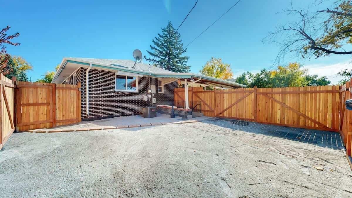 A single-story brick house with a fenced backyard, a satellite dish, and a wooden gate.