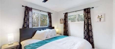 A bedroom with a bed, curtains, a ceiling fan, and a window.