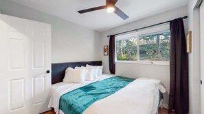 Quarto com cama, ventoinha no teto, janela com cortinas e porta.
