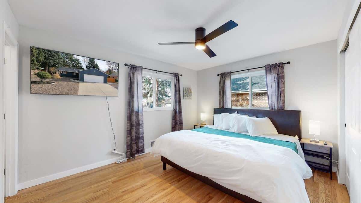 A bedroom with a bed, a ceiling fan, a window with curtains, and a wall-mounted TV.