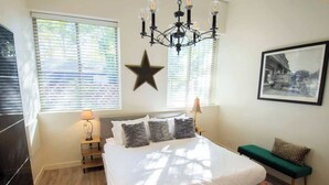 Quarto com uma cama grande, duas luminárias de cabeceira, um adorno em forma de estrela, uma moldura com imagem e um banquinho.