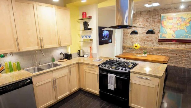 A modern kitchen with light wooden cabinets, a black stove, and a map on the wall.
