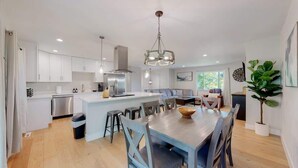 Una cocina moderna con armarios blancos, una isla central y un comedor con sillas azules.