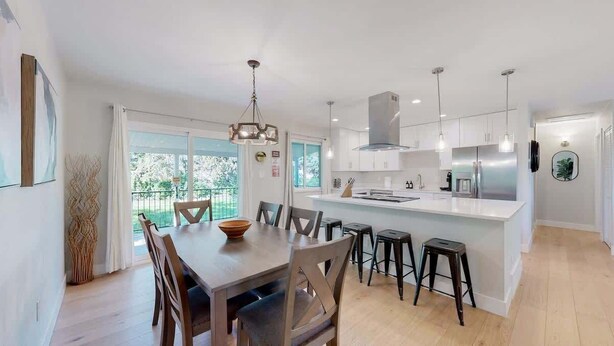 Una cocina moderna con armarios blancos, una isla central y un comedor con sillas y mesa de madera.
