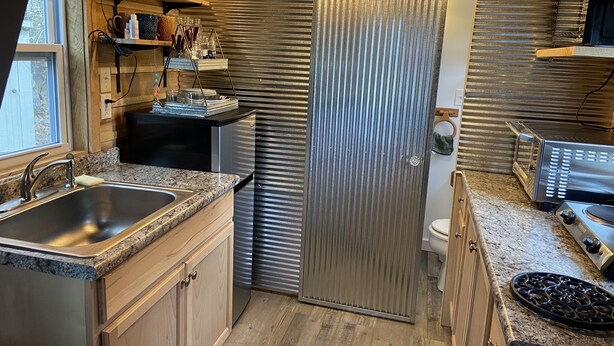 A compact kitchen with a stainless steel refrigerator, granite countertops, and a wooden backsplash.