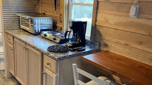 A compact kitchen with wooden cabinets, a built-in stove, a coffee maker, and a window overlooking a snowy landscape.