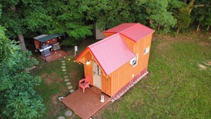 A small wooden cabin with a red roof, a porch, and a grill area.