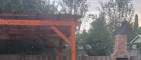 A backyard with a brick patio, a wooden table, a brick barbecue, and a brick oven.
