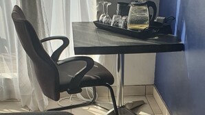 Ein Hotelzimmer mit Bett, Schreibtisch, Wasserkocher, Gläsern und Stuhl.