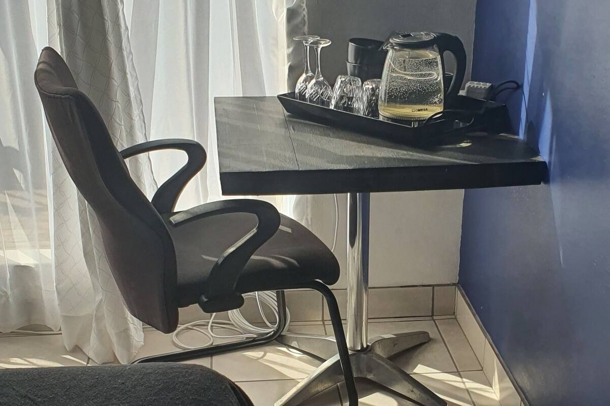 Habitación de hotel con cama, escritorio, tetera, vasos y una silla.