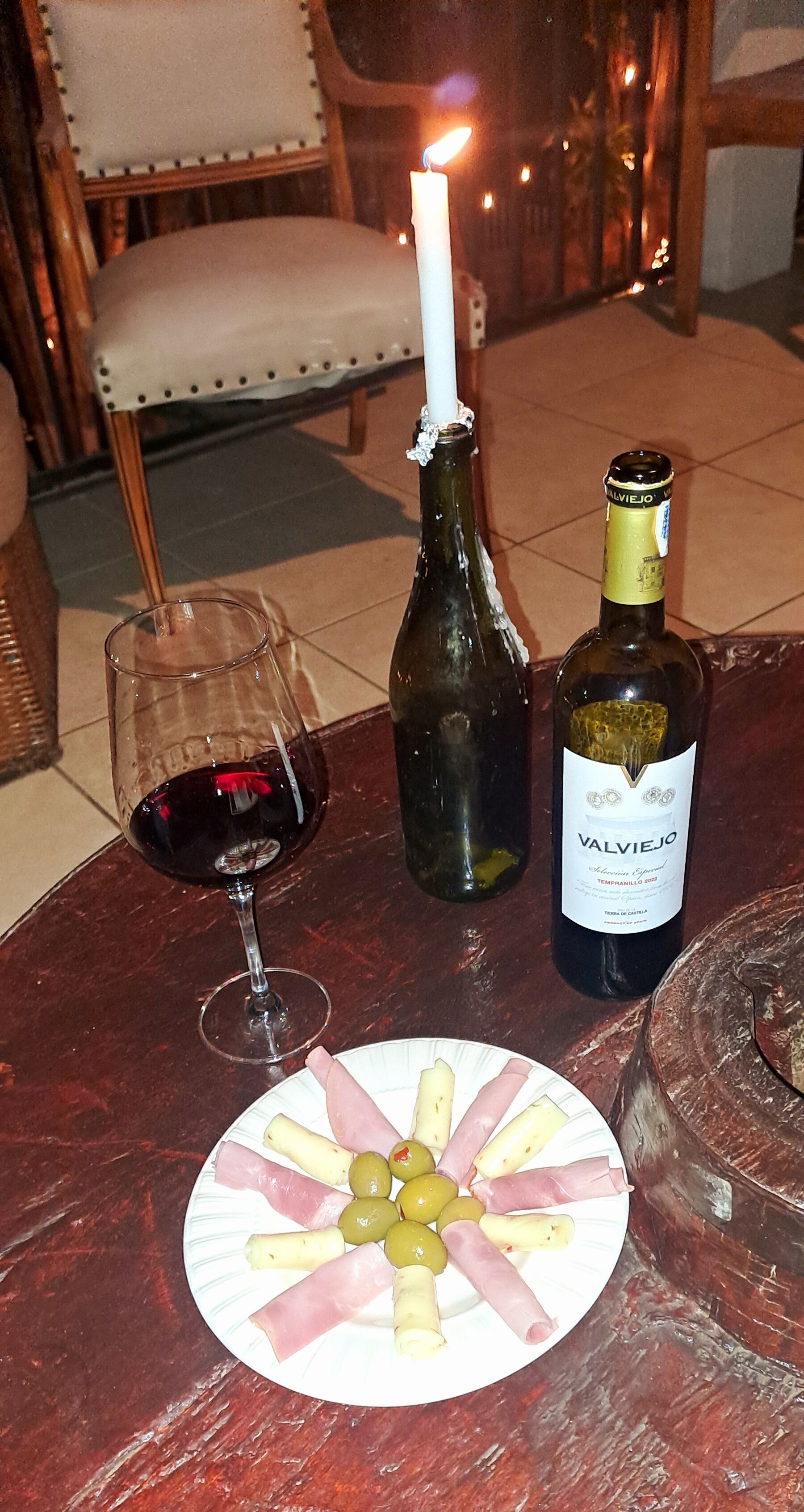 A table with a bottle of wine, a glass of red wine, and a plate of food.