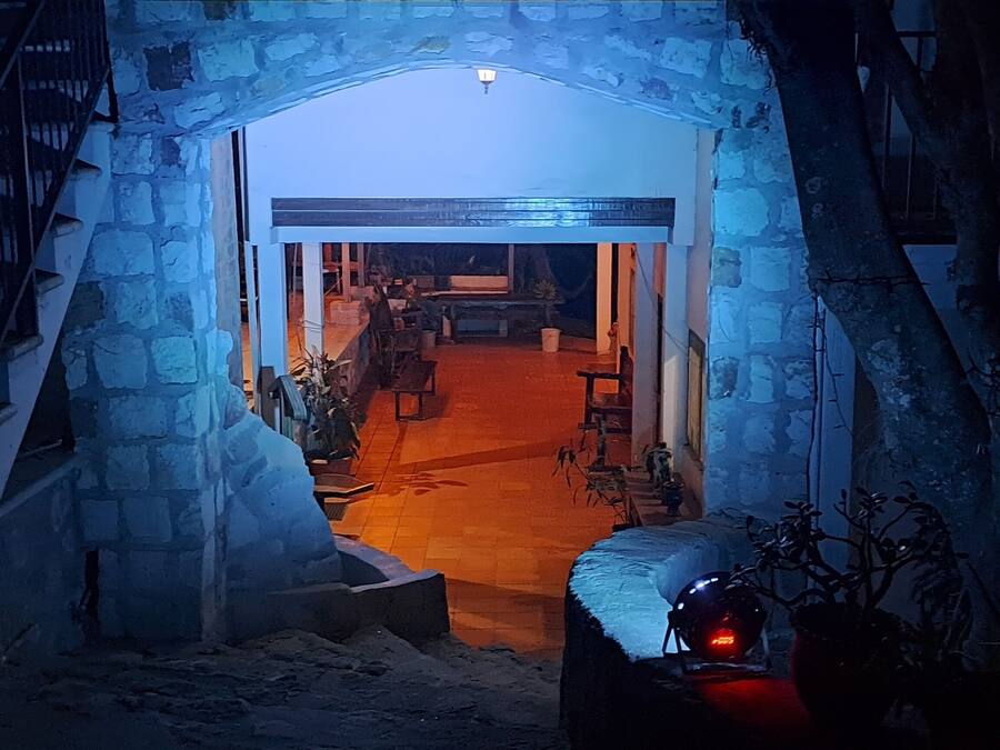 An entrance to a building with a stone archway, a staircase on the left, and a red-lit interior visible through the archway.
