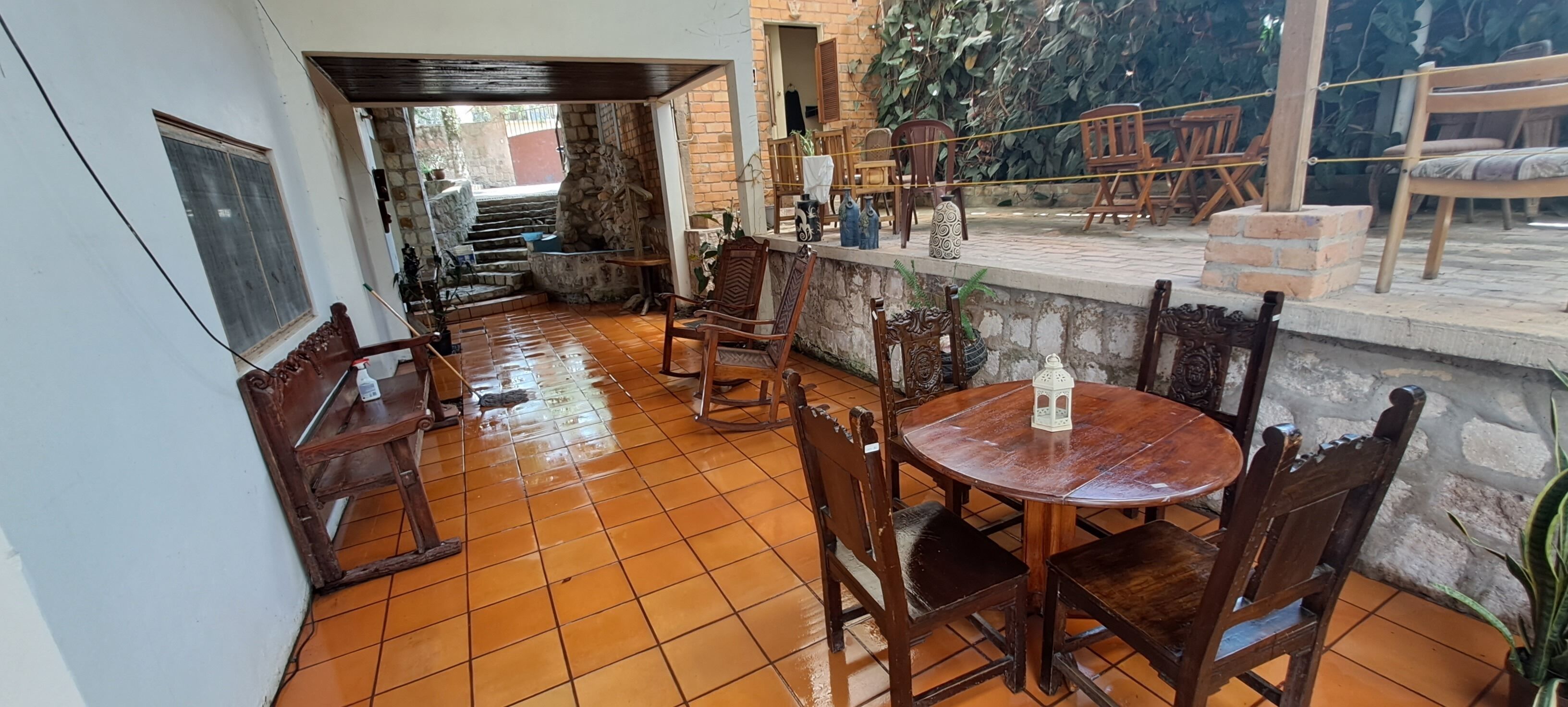 Un patio con una mesa redonda de madera y sillas, una escalera de piedra y varios muebles de madera.