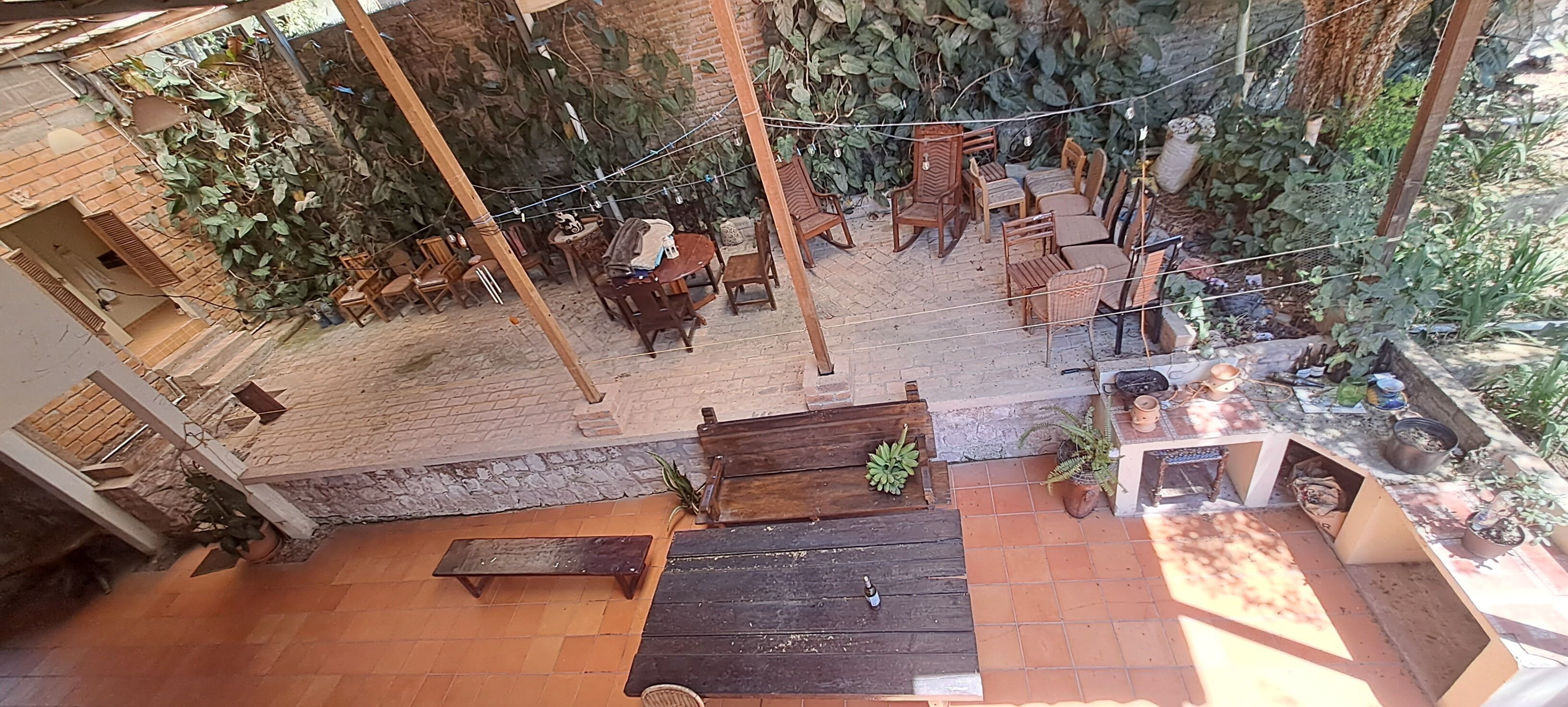 Un patio al aire libre con mobiliario de madera, incluyendo una mesa redonda y sillas, además de un banco de madera.
