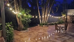 An outdoor patio with a tiled floor, a table with chairs, string lights, and potted plants. - Villa Chelsey (Valle de Angeles)