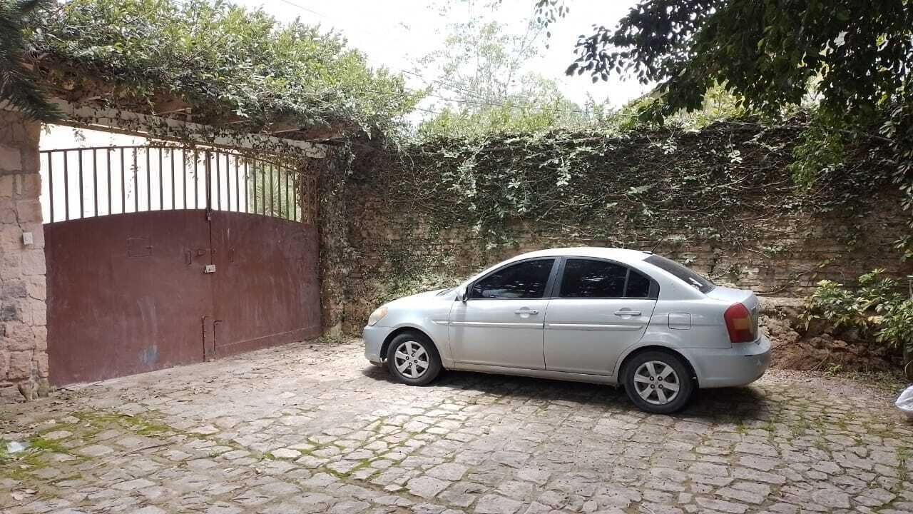 A silver car parked in front of a gated area with a stone-paved driveway.