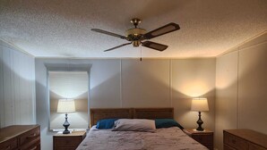 Una camera da letto con un letto, due comodini con lampade, una ventola a soffitto e una finestra con persiane.