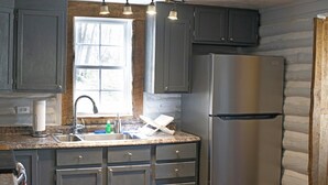 A kitchen with dark cabinets, a stainless steel refrigerator, a granite countertop, and a window with a view of trees.