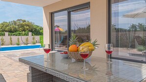 Une table en verre sur laquelle se trouvent un panier de fruits et deux verres à vin, avec vue sur une piscine.