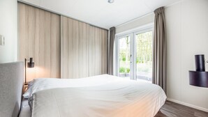 A modern hotel room with a large bed, a bedside table, a lamp, a TV, and a view of greenery through the window. - Nice home in Zorgvlied with WiFi (Zorgvlied)