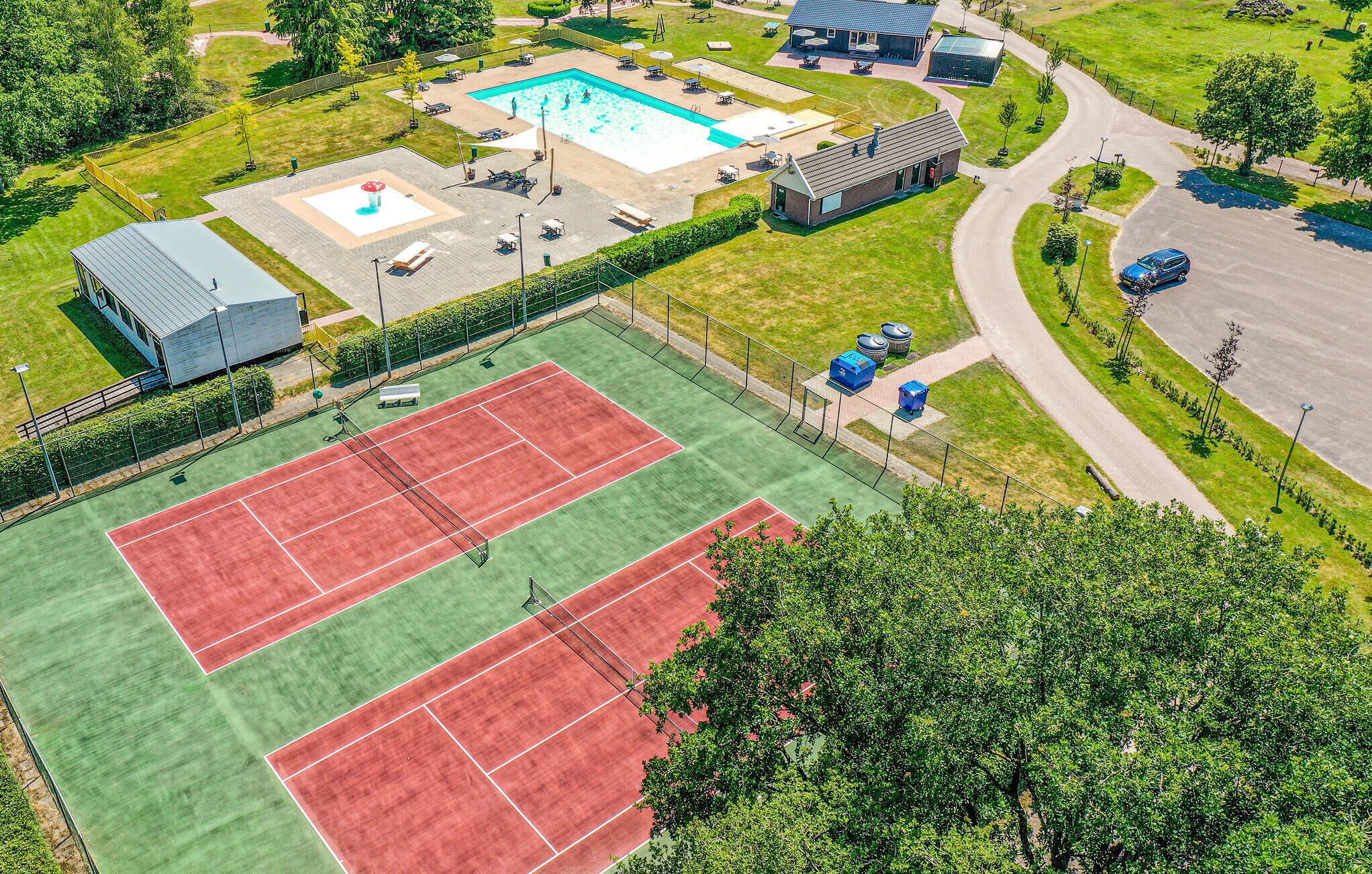 An aerial view of a sports facility with a swimming pool, tennis courts, and a small building.