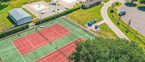 An aerial view of a sports facility with a swimming pool, tennis courts, and a small building.