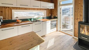 A modern kitchen with wooden paneling, a large window, and a wood-burning stove. - Stunning home in ålen (Ålen)