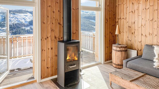 A cozy room with a wood-paneled interior, a fireplace, a sofa, and a view of a snowy landscape through large windows. - Stunning home in ålen (Ålen)