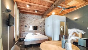 Une chambre avec un plafond en bois, un mur en briques, un lit, une table ronde en bois et un miroir.