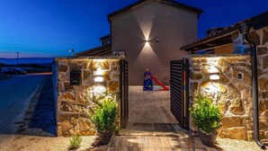 A stone entrance with a metal gate, a small play area with a slide, and a building with a sloped roof. - Luxurious home in Benkovac (Benkovac)