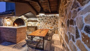 An outdoor patio with a stone wall, a brick oven, and a wooden table with chairs. - Luxurious home in Benkovac (Benkovac)