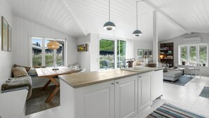 Una cucina moderna con mobili bianchi, un piano di lavoro in legno, illuminazione a sospensione e vista sull'esterno.