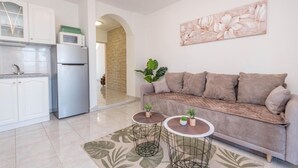 A modern apartment with a kitchenette, a sofa, two round tables with plants, and a large floral artwork on the wall.