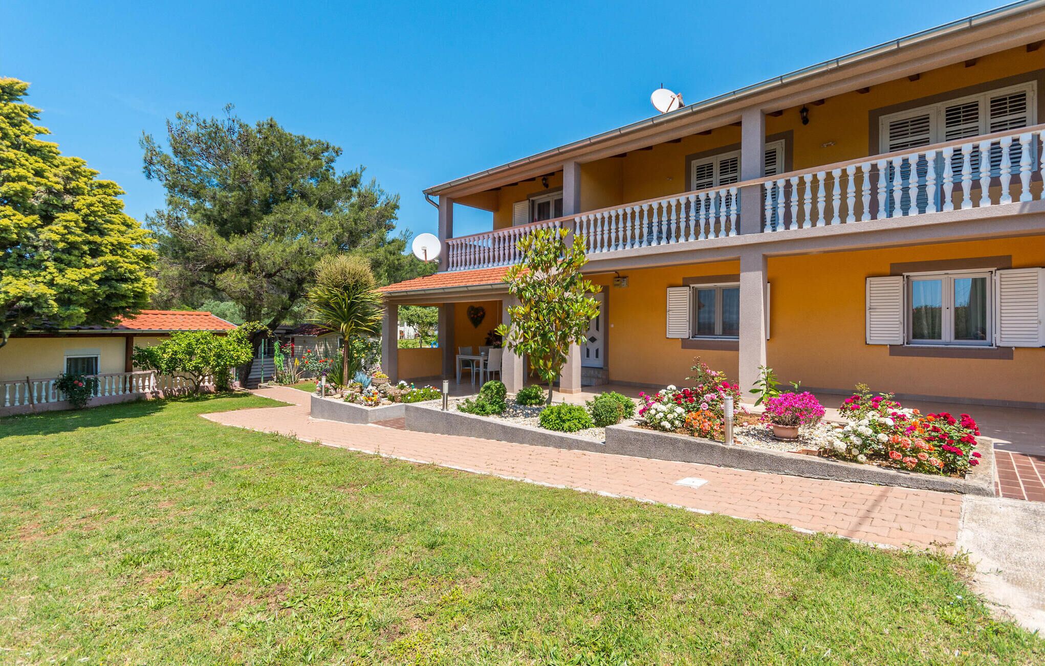Un edificio a due piani con un balcone, un giardino fiorito e un cielo azzurro limpido.
