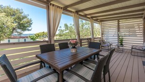 Un patio techado al aire libre con mesa de madera y sillas de mimbre, con vista a una piscina y árboles.