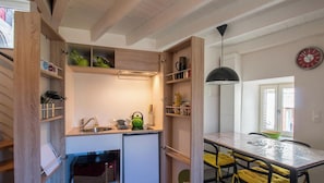 A compact kitchen with built-in shelves, a refrigerator, and a dining area with a table and chairs.