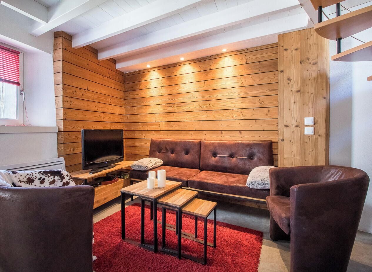 A cozy living room with a wooden wall, a leather sofa, a TV, and a red rug.