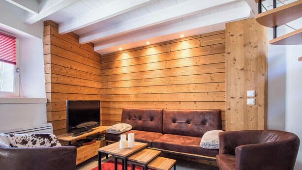 Una sala de estar acogedora con una pared de madera, un sofá de cuero, un televisor y una alfombra roja.