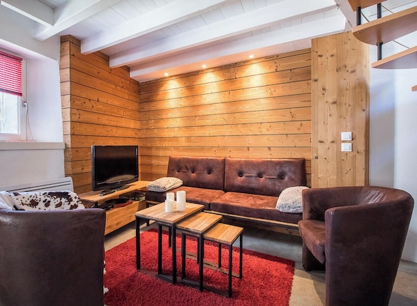 Una sala de estar acogedora con una pared de madera, un sofá de cuero, un televisor y una alfombra roja.