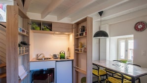 Cocina compacta con electrodomésticos integrados, estantes de madera y comedor con sillas amarillas.