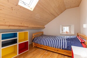A bedroom with a sloped ceiling, a bed with a striped bedspread, a window with a view, and a built-in storage unit with multiple compartments.