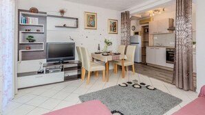A modern living room with a flat-screen TV, a dining table with chairs, a kitchen area with cabinets and appliances, and a decorative rug. - 1 bedroom cozy apartment in Vir (Vir)