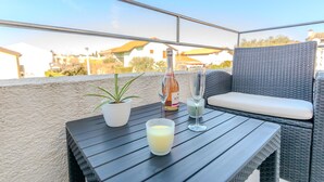 A balcony with a wicker sofa, a small potted plant, a bottle of wine, and two glasses. - 1 bedroom cozy apartment in Vir (Vir)