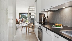 Une cuisine moderne avec des armoires blanches, un comptoir noir et des appareils en acier inoxydable. On aperçoit un coin repas avec une table et des chaises à travers une porte-fenêtre coulissante.