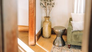 A room with a wooden floor, a green sofa, a patterned rug, a vase with dried plants, and framed pictures on the wall. - 3 Min to downtown & Falls Park, 10 min to Airport - Clean King Bed Home (Sioux Falls)