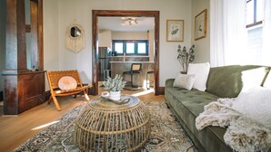 A living room with a green sofa, a wicker coffee table, a patterned rug, and a wooden door. - 3 Min to downtown & Falls Park, 10 min to Airport - Clean King Bed Home (Sioux Falls)