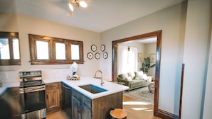 A modern kitchen with a central island, stainless steel appliances, wooden cabinetry, and a large window. - 3 Min to downtown & Falls Park, 10 min to Airport - Clean King Bed Home (Sioux Falls)