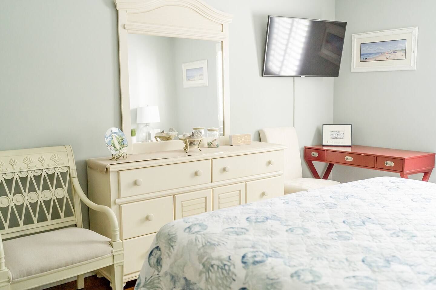 Une chambre à coucher comprenant un lit, une commode, une coiffeuse, un miroir, un téléviseur et un tableau encadré accroché au mur.